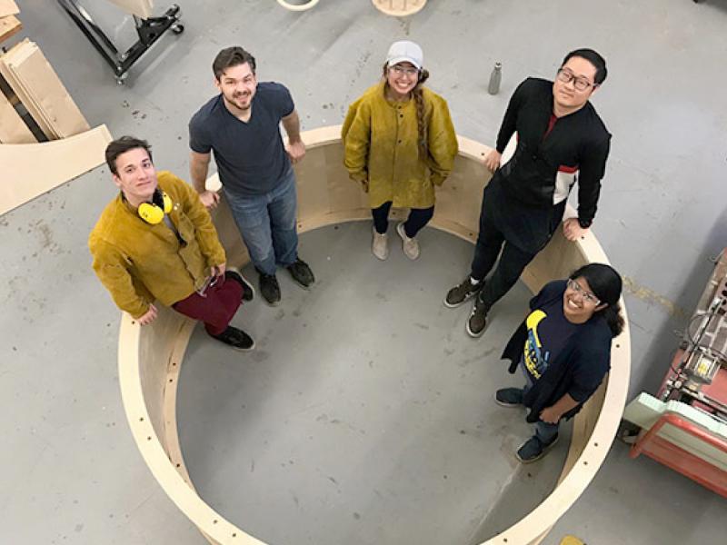 Students pose inside a gigantic wheel they fabricated.