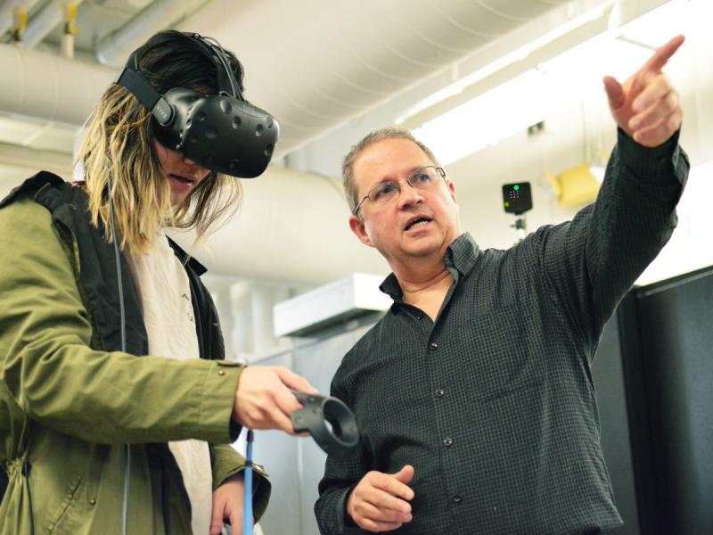 A professor points as a student wears a virtual reality headset.