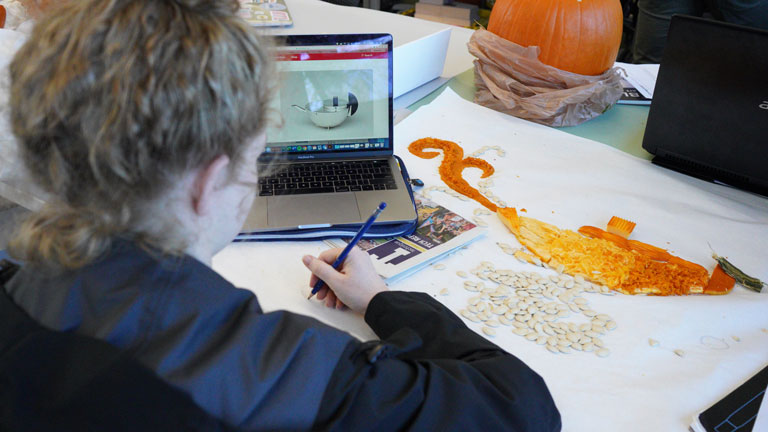 A student uses pumpkin parts to create an image for her pumpkin’s design poster, based off a Bauhaus teapot.