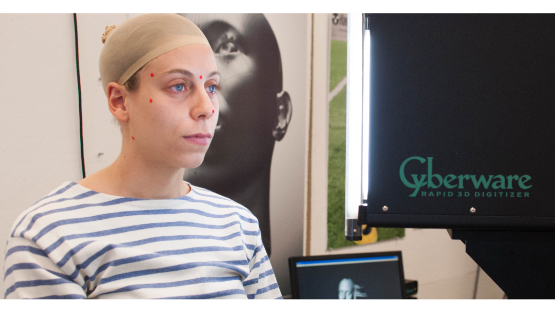 A student wears red dots on her face as she is scanned by a 3-D scanning machine.